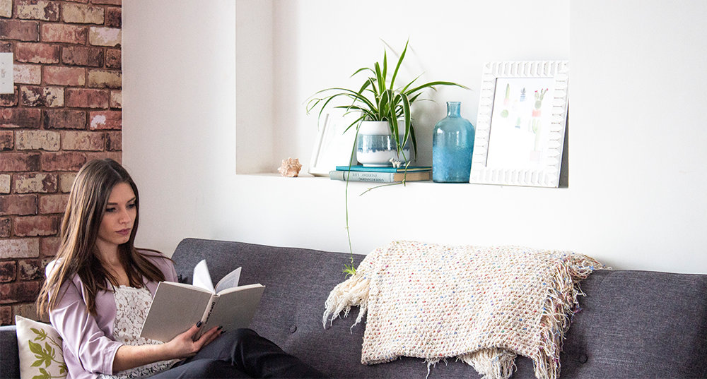 young woman reading book with plant shelfie behind